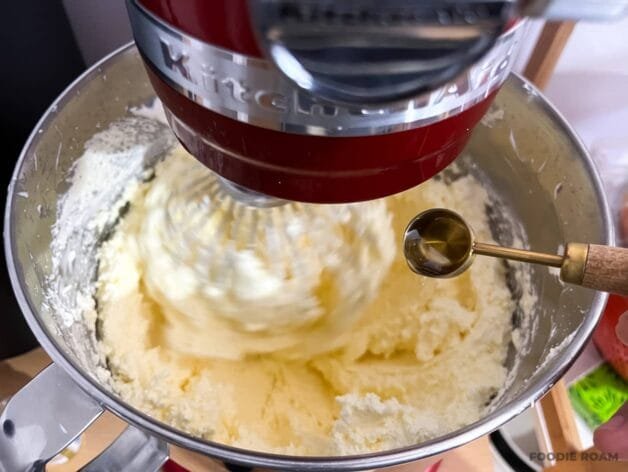 Almond extract being added to the buttercream mixture in a stand mixer.