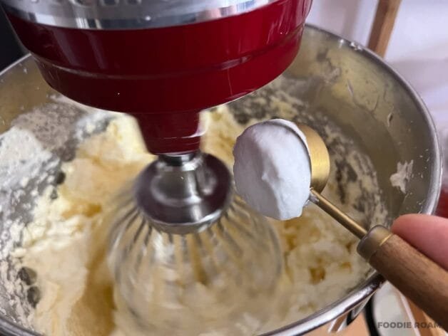 Coconut milk being added to the buttercream mixture in a stand mixer.