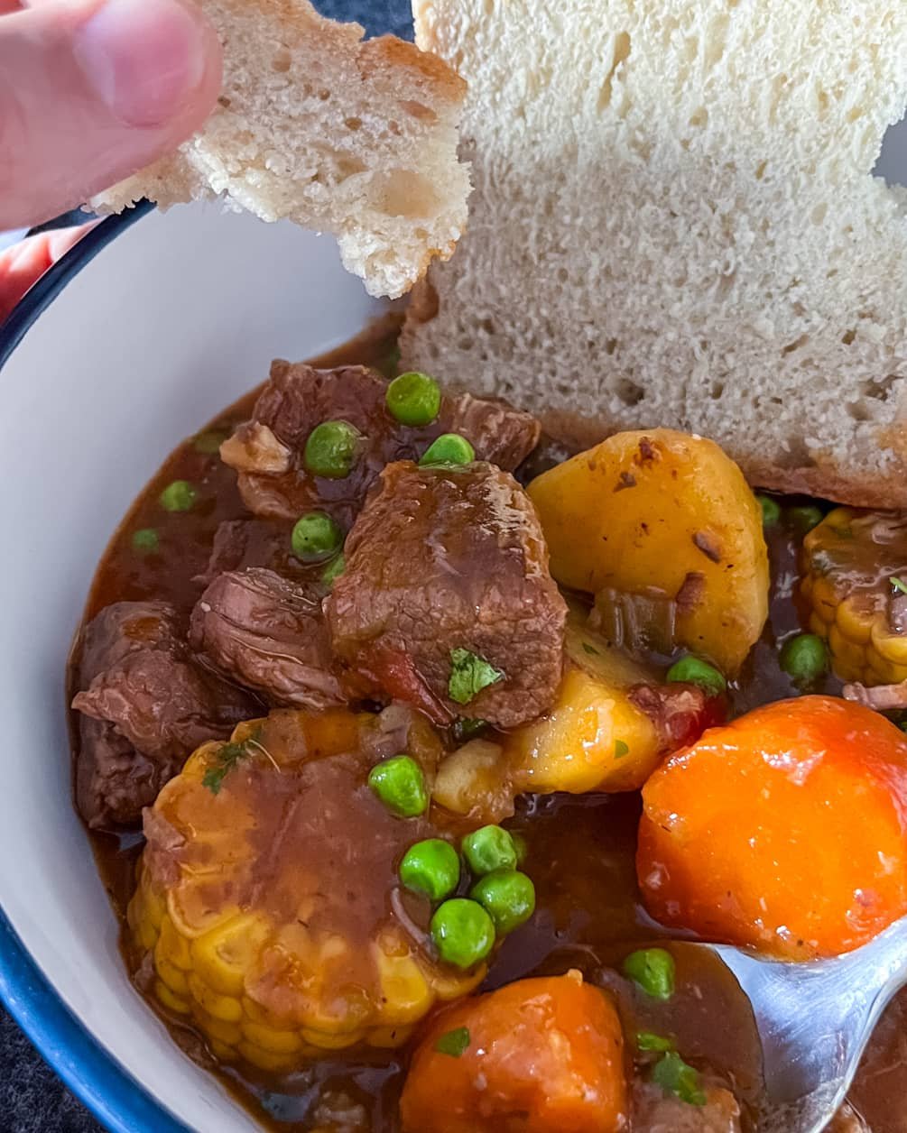 Bowl of Guinness beef stew with tender beef chunks, potatoes, carrots, corn, and peas, served with crusty bread.