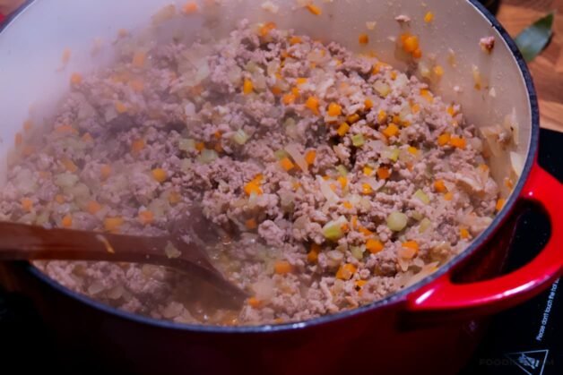 Seasoned pork and beef browning in a large pot, being broken into smaller pieces with a wooden spoon to build the foundation of a rich meat ragu.