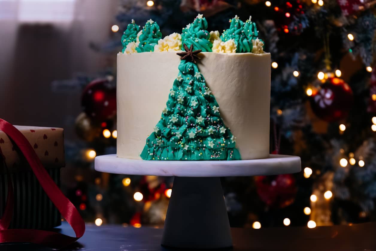 A festive Coconut Almond Cake decorated with a green buttercream Christmas tree design, topped with colorful sprinkles and a star anise.