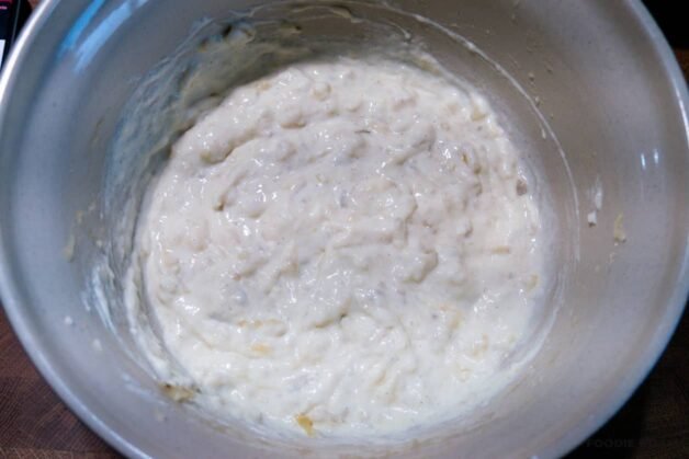 A glass bowl with mashed bananas, sour cream, and vanilla being stirred with a spoon.