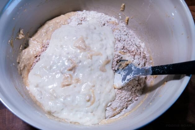 A mixing bowl with banana bread batter being combined, showing wet ingredients on top of the dry ingredients.