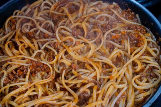 Linguine pasta tossed with rich Dalmatian-style meat ragu in a pan, cooking gently to absorb the sauce and reach the perfect al dente texture.