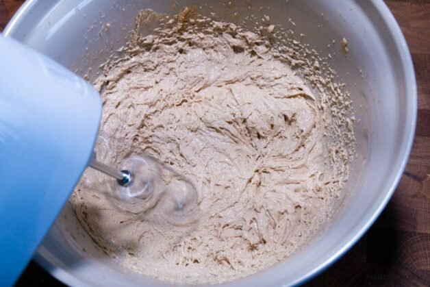 A bowl of browned butter and light brown sugar being mixed with a hand mixer.