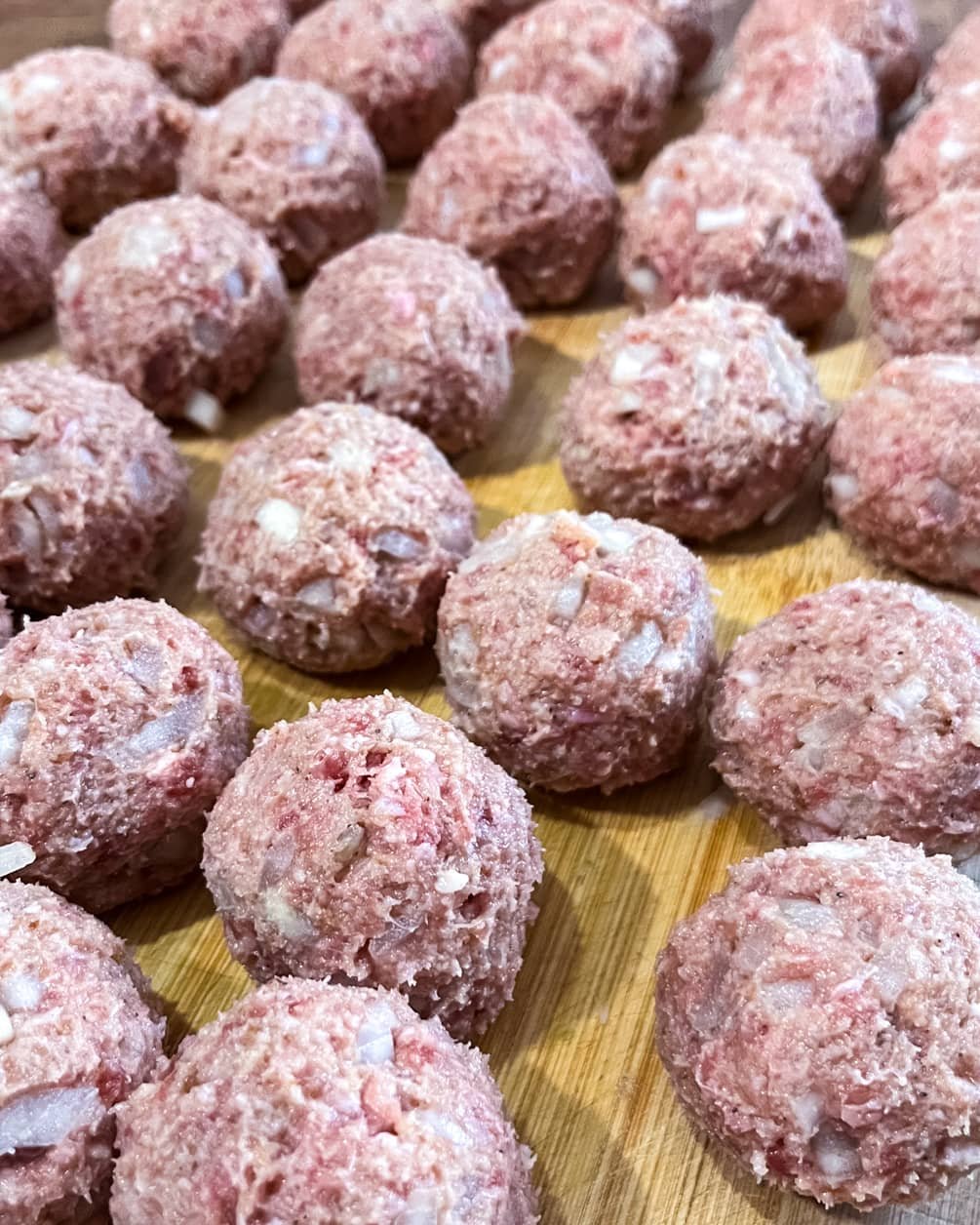 Raw homemade meatballs with finely chopped onions, neatly arranged on a wooden board, ready for cooking.