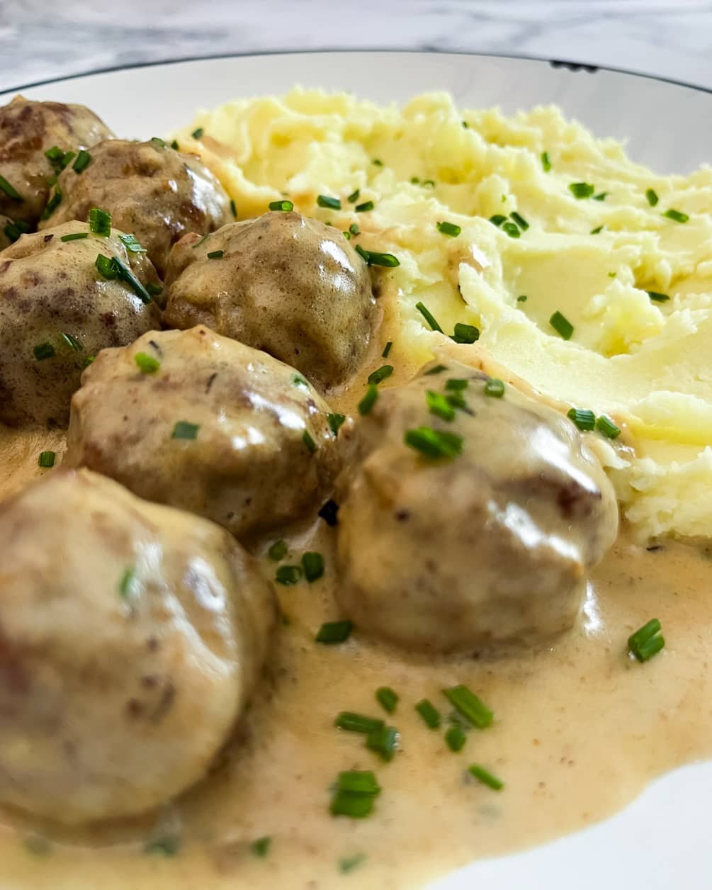 Creamy meatballs served in a rich sauce, paired with fluffy mashed potatoes, and garnished with fresh chives.