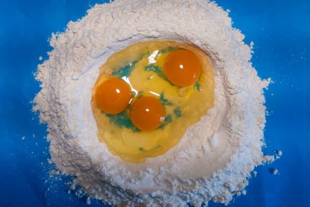 A mound of flour with three cracked eggs in the center, ready to be mixed for homemade pasta dough.