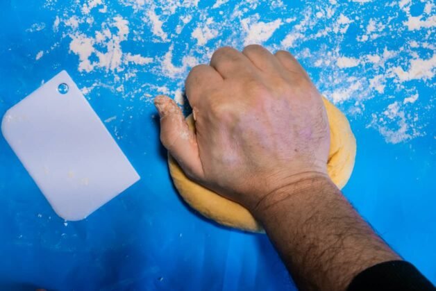 A hand kneading pasta dough on a floured surface, creating a smooth and elastic texture.