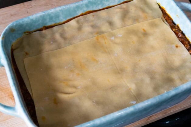 Fresh pasta sheets layered evenly over a bed of meat ragu in a baking dish.