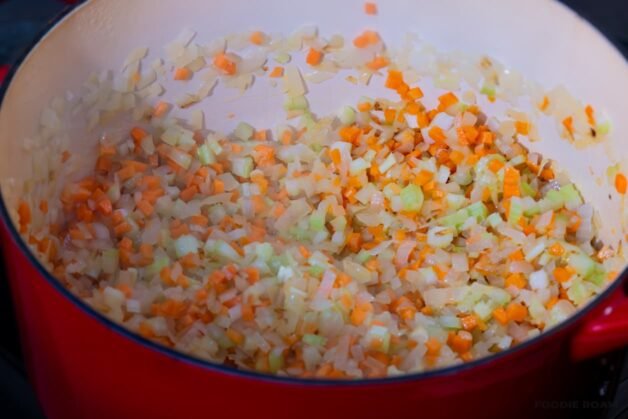 Onions, carrots, and celery sautéing in a large pot with olive oil, releasing their aroma and creating the flavor base for Dalmatian-style meat ragu.