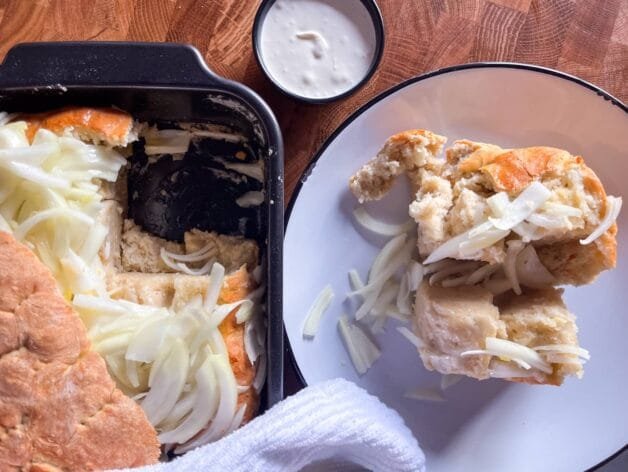 A serving of onion flatbread on a white plate with sour cream on the side.