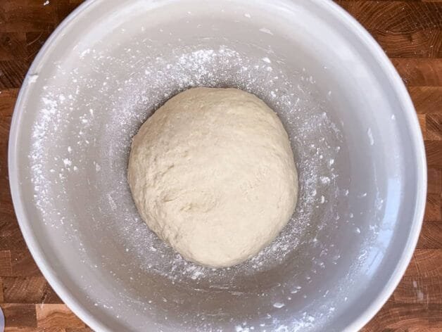 Flatbread dough resting in a white bowl, lightly dusted with flour.