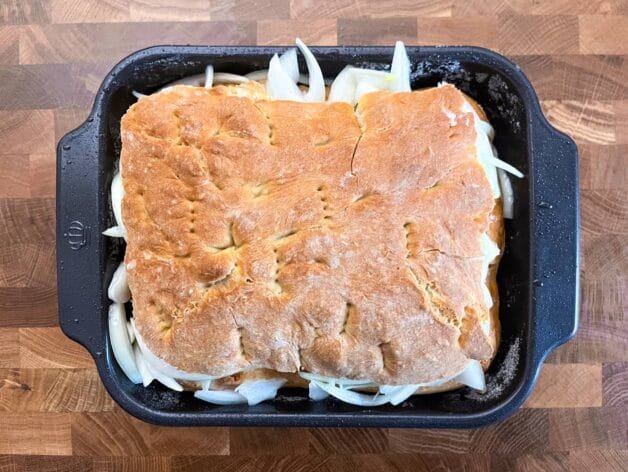 Baked onion flatbread with a golden top crust in a black baking pan.