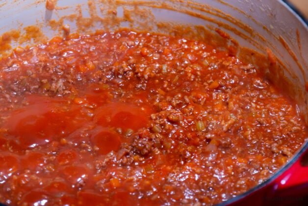 A pot of Dalmatian-style meat ragu simmering gently on low heat, partially covered with a lid, with steam escaping as the sauce thickens.