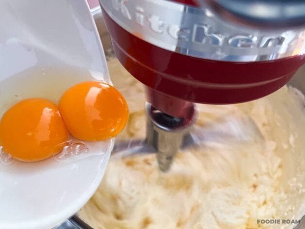 One whole egg being added to a stand mixer with a creamy butter and sugar mixture.
