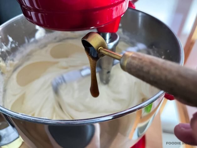 Vanilla extract being poured into the cake batter in a stand mixer.