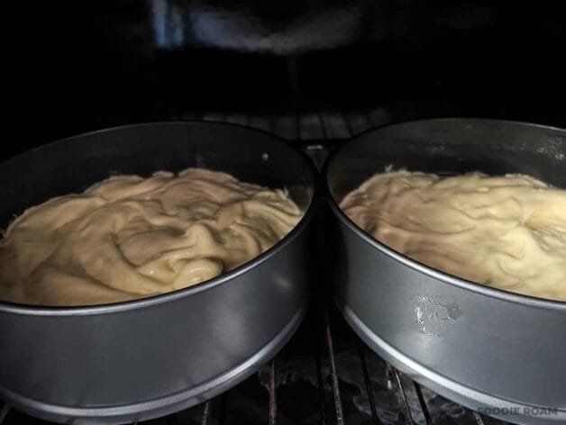 Two cake pans filled with batter placed in the oven, beginning to bake.