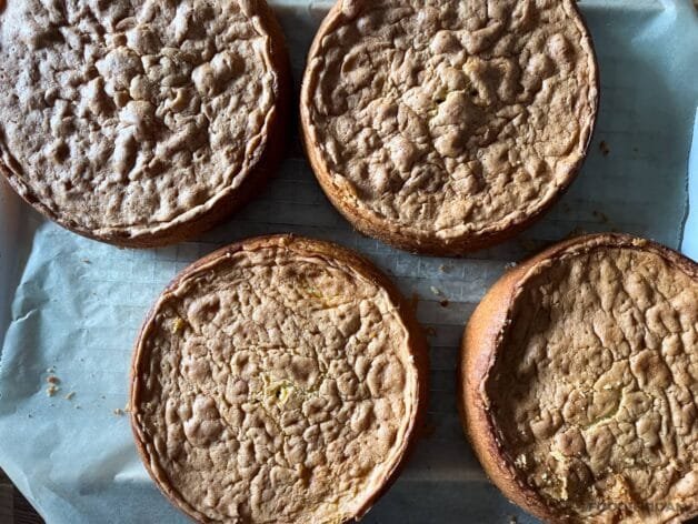 Four baked coconut cake layers cooling on a wire rack.