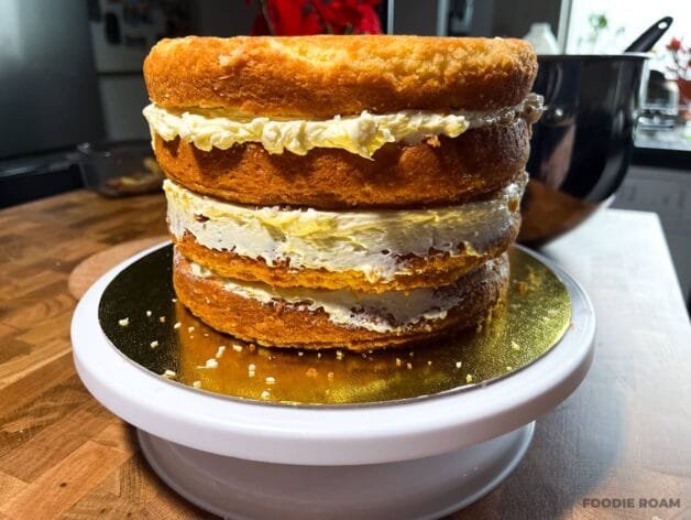 Four cake layers stacked with buttercream filling between each layer on a cake stand.
