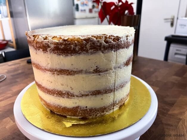 Crumb-coated cake with a thin layer of buttercream on a rotating cake stand.