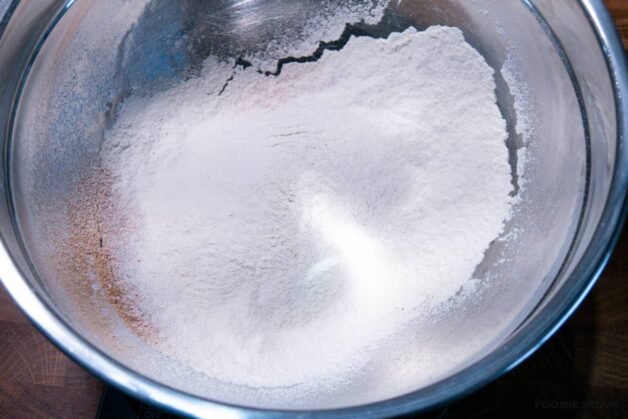 A bowl with flour, cinnamon, salt, and baking soda being whisked together with a whisk.