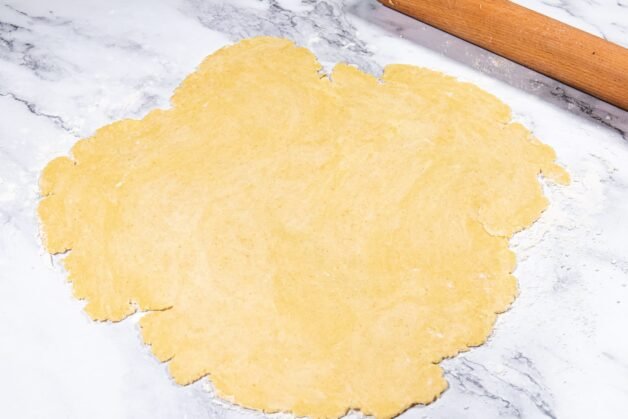 Rolled-out pie dough on a floured surface, ready to be placed in the pie dish.