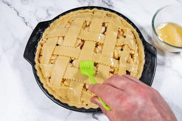 Applying egg wash to the lattice crust of an apple pie before baking.