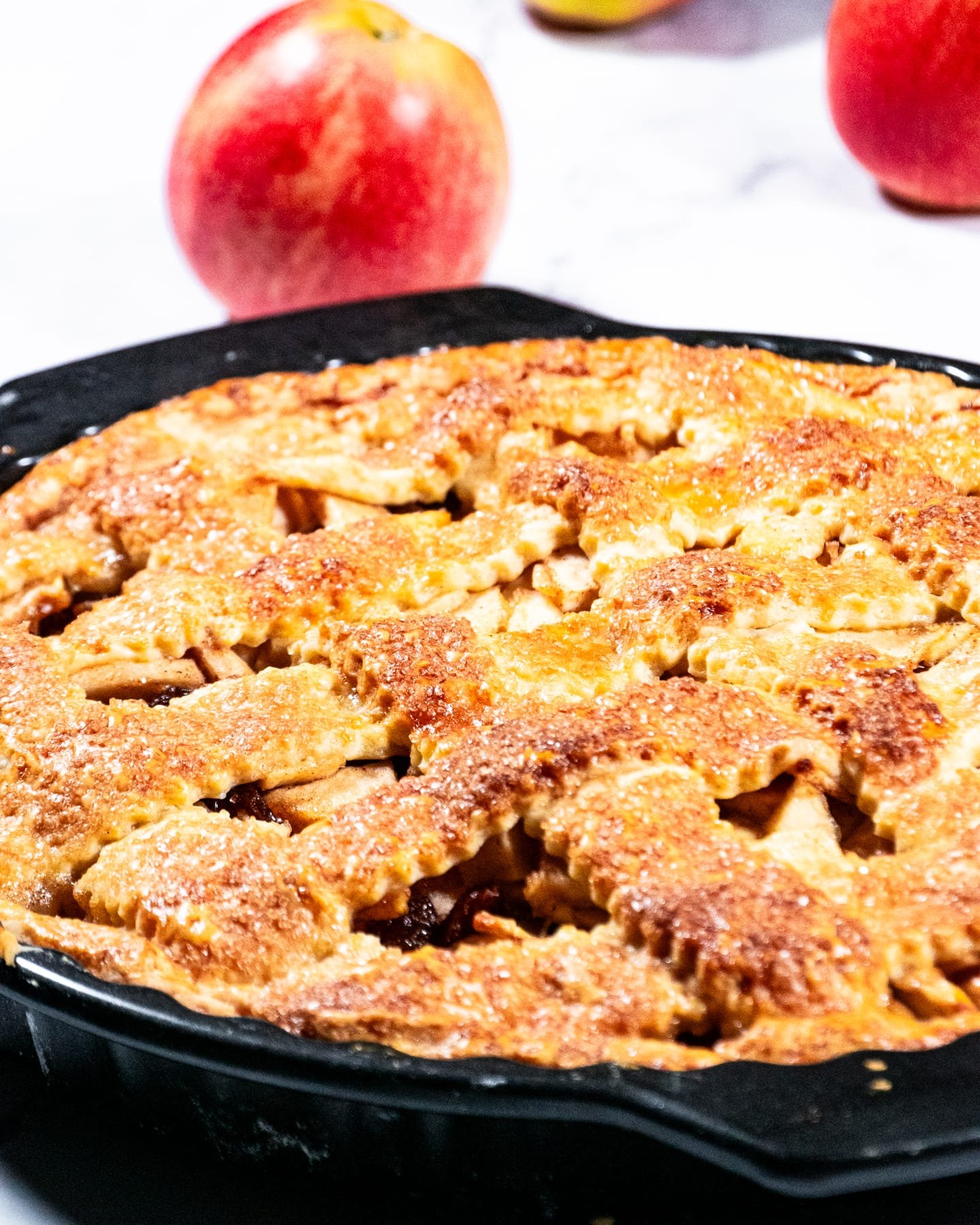 A freshly baked apple pie with a golden-brown crust, surrounded by red apples.