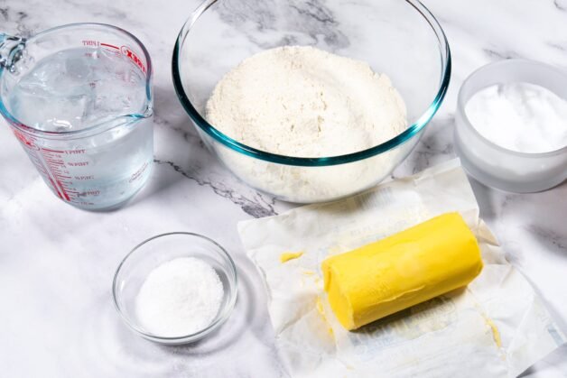 Ingredients for the perfect pie crust, including flour, butter, sugar, salt, and a cup of cold water.