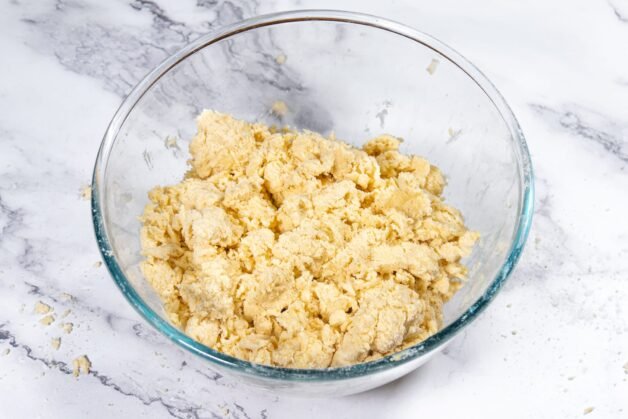 A bowl of pie crust dough with visible flaky layers, ready to be wrapped and chilled.