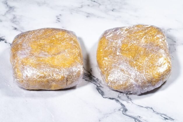Two portions of pie dough wrapped in plastic wrap, ready to be chilled.