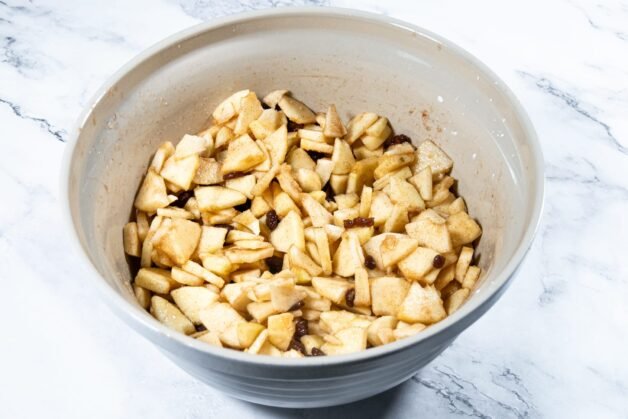 Apple slices mixed with sugar, cinnamon, and raisins in a bowl, ready for the pie filling.