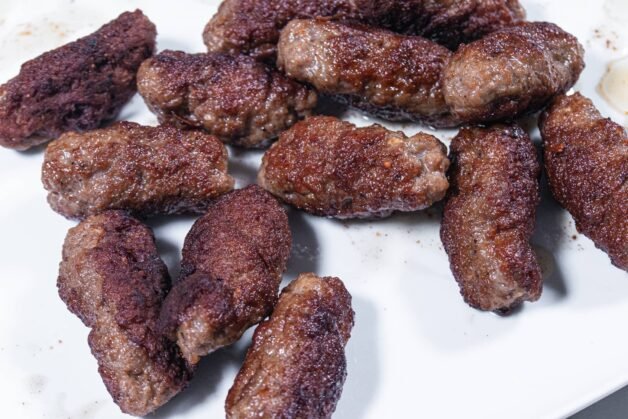 Juicy grilled cevapi on a white plate, freshly cooked and golden brown.