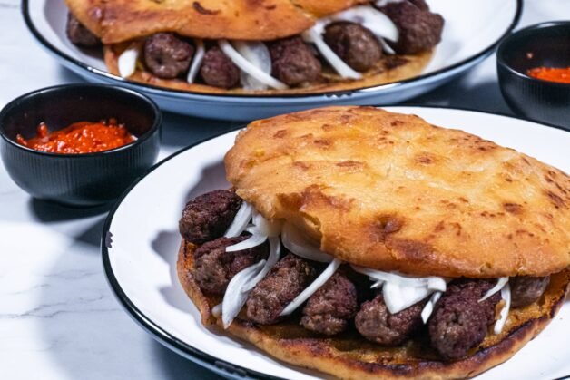 Cevapi sandwich served on golden flatbread with onions and ajvar