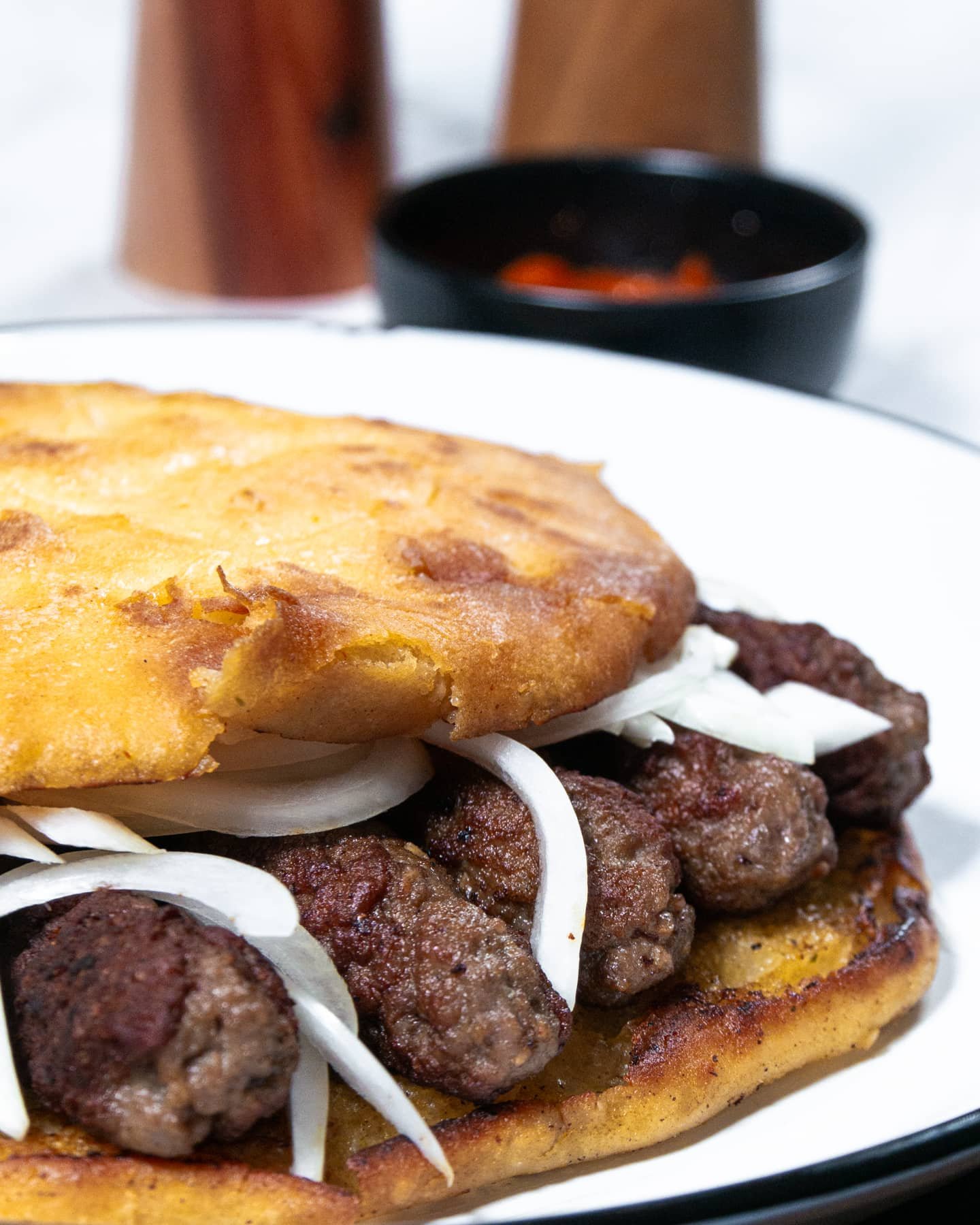 Traditional Balkan cevapi sandwich with grilled meat rolls, fresh onions, and golden flatbread.