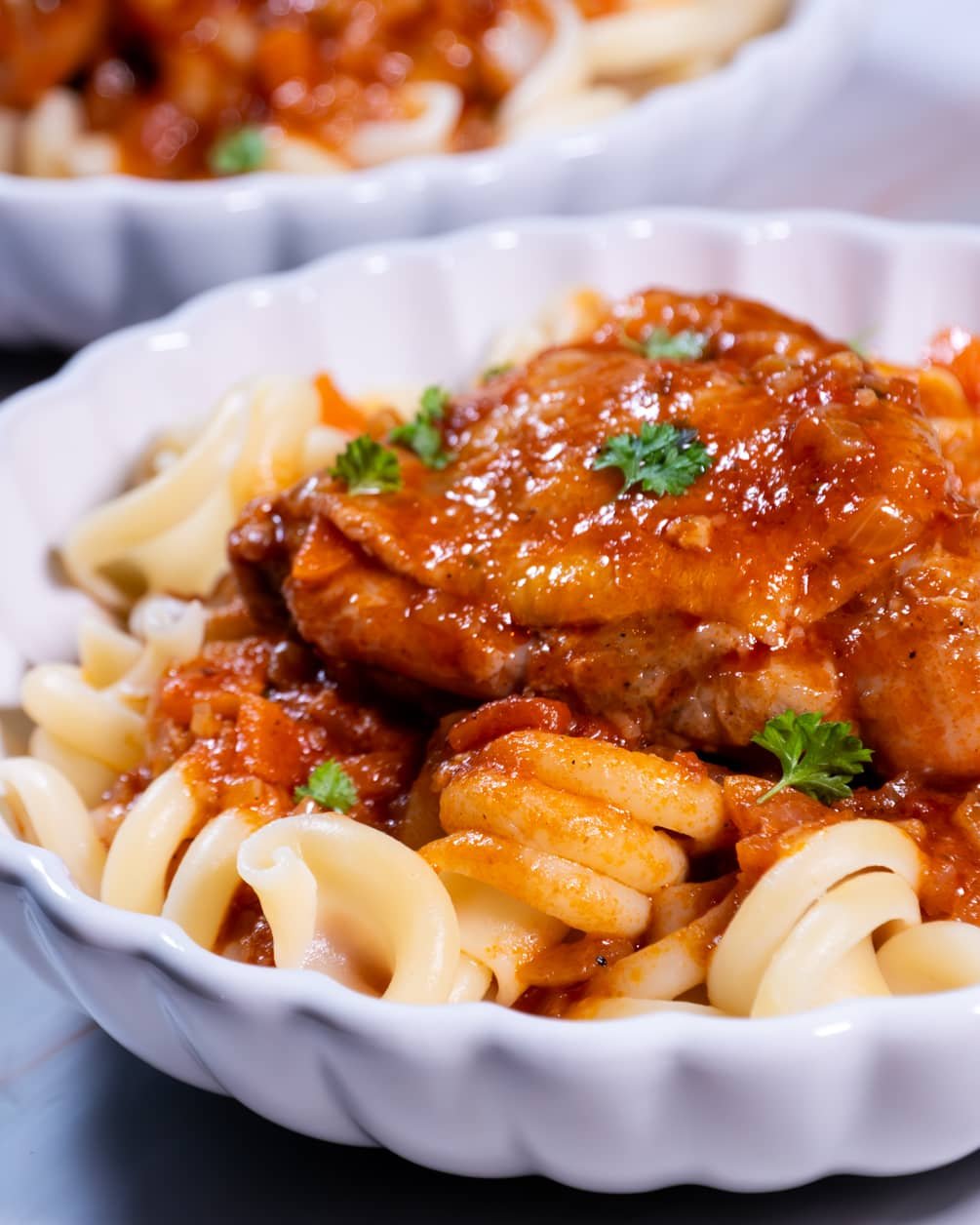 Close-up of chicken in tomato sauce served over pasta, garnished with parsley.