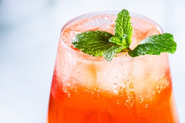 A close-up of a Citrus Hennessy Spritz cocktail garnished with fresh mint leaves, highlighting the vibrant orange color and ice cubes.