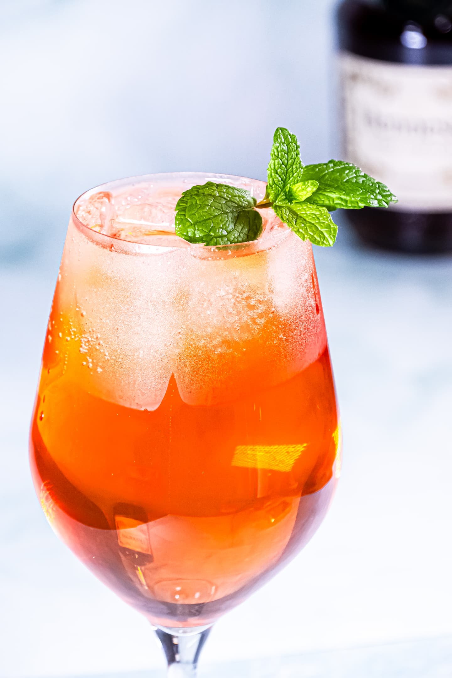 A vibrant Citrus Hennessy Spritz cocktail served in a large glass, garnished with fresh mint leaves, against a light background.