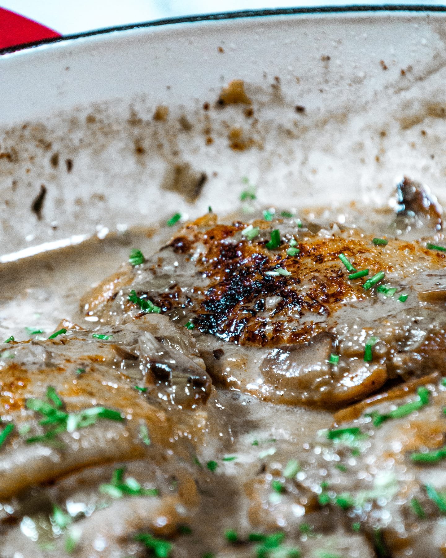 Close-up of crispy, golden chicken thighs simmered in a creamy mushroom and leek sauce with fresh chive garnish.