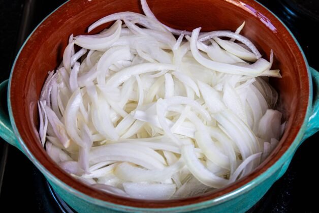Fresh sliced onions in a ceramic pot ready for cooking.
