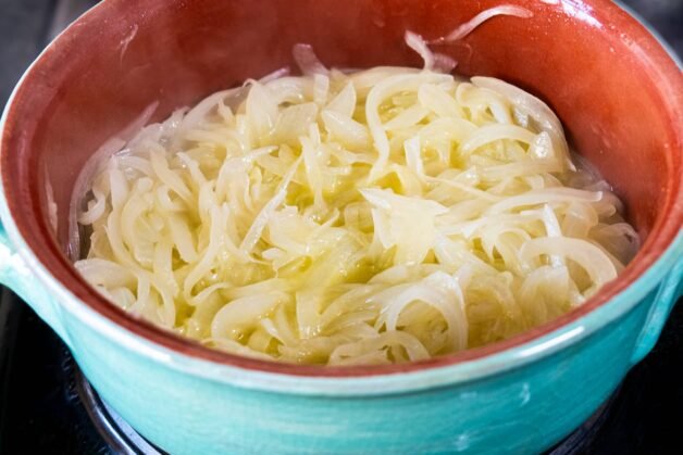Onions starting to soften in a ceramic pot.