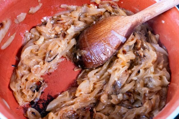 Caramelized onions in a pot with a wooden spoon.