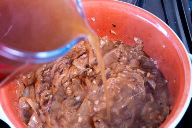 Pouring beef broth into caramelized onions.