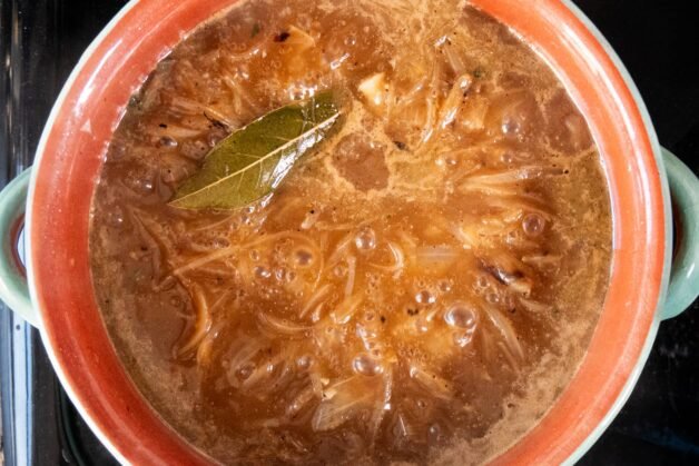 French onion soup simmering with a bay leaf.