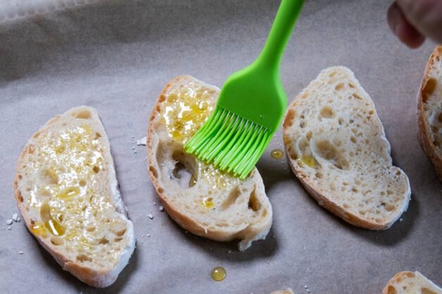 Brushing olive oil on baguette slices.