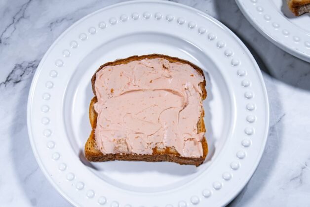 A slice of toast spread with creamy salmon-flavored cream cheese on a white plate.