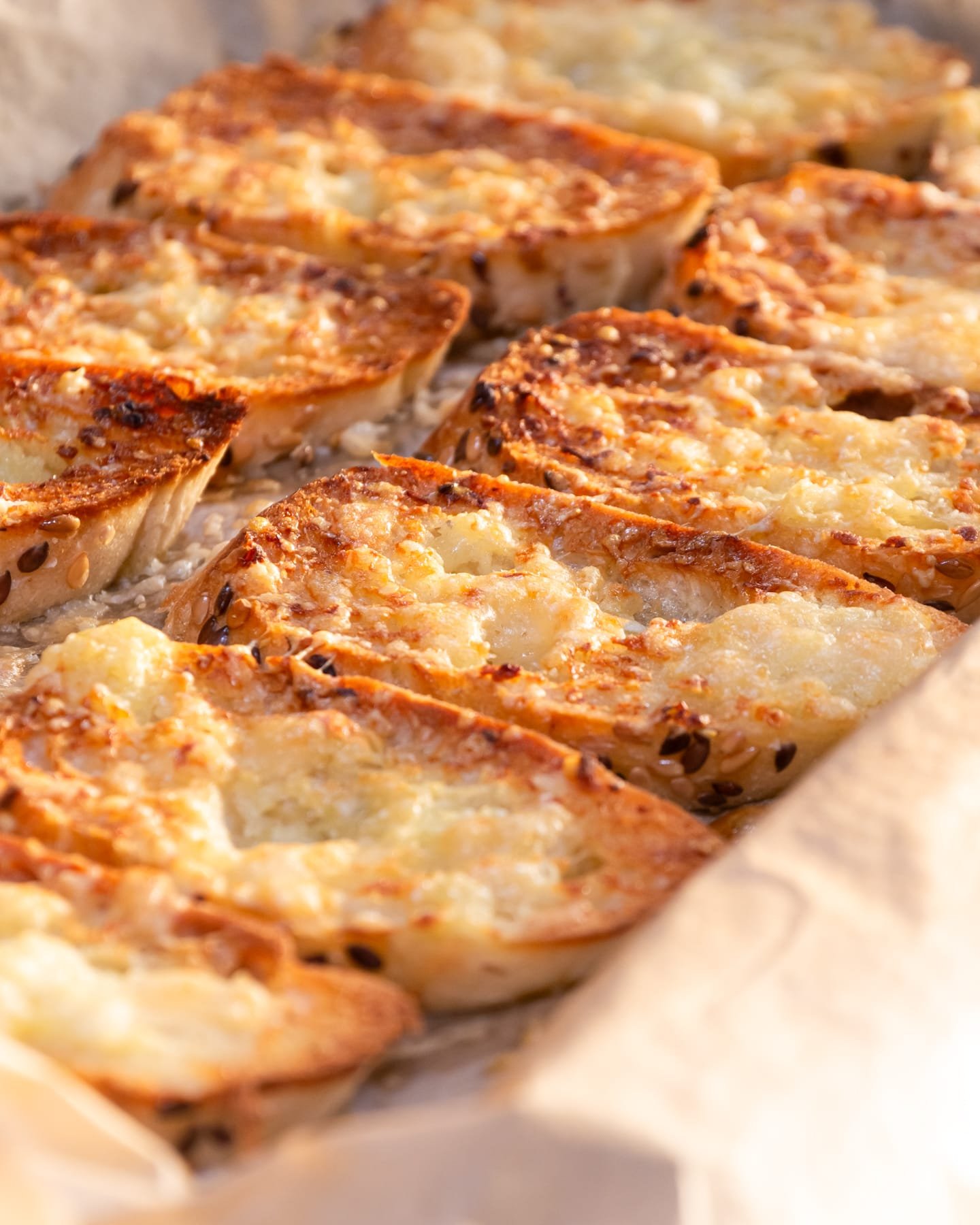 Golden garlic bread slices on a baking sheet with melted cheese topping.