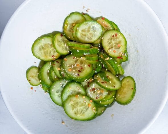 Korean cucumber salad (Oi Muchim) in a white bowl, garnished with sesame seeds and chili flakes.