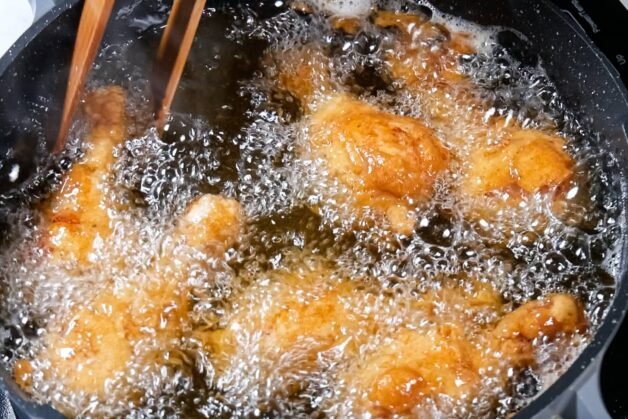 Golden-brown chicken drumsticks frying in hot oil, surrounded by bubbling oil.